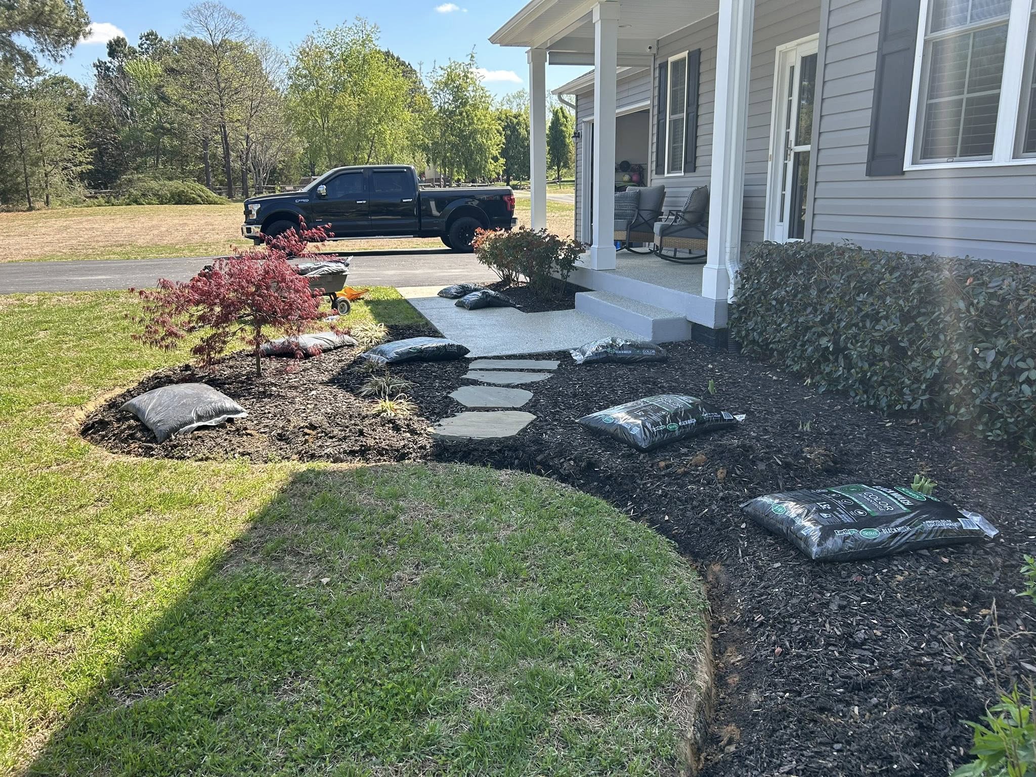 Landscaped garden bed with black mulch, stone stepping path, and Japanese maple at a home