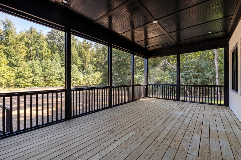 Screened porch with light wood deck flooring, black railings, and dark beadboard ceiling
